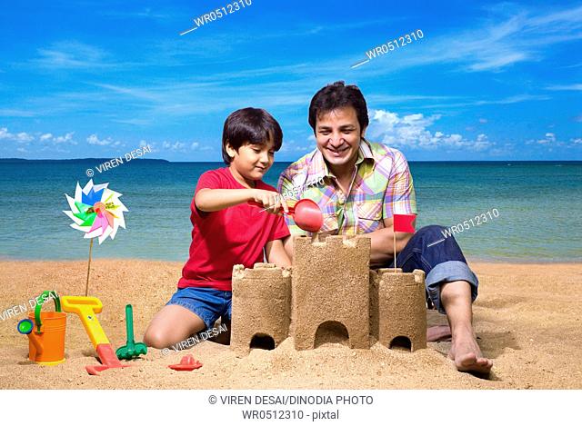Father with son pouring sand on sandcastle at seashore MR779H, 779G