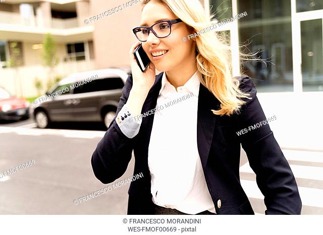 Portrait of smiling young businesswoman on the phone crossing street
