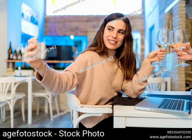 Woman taking selfie through smart phone while raising toast at restaurant