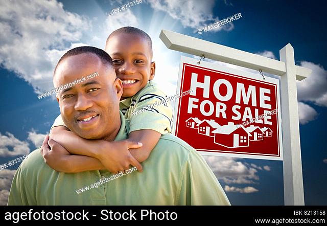 Happy african american father with son in front of home for sale real estate sign and sky