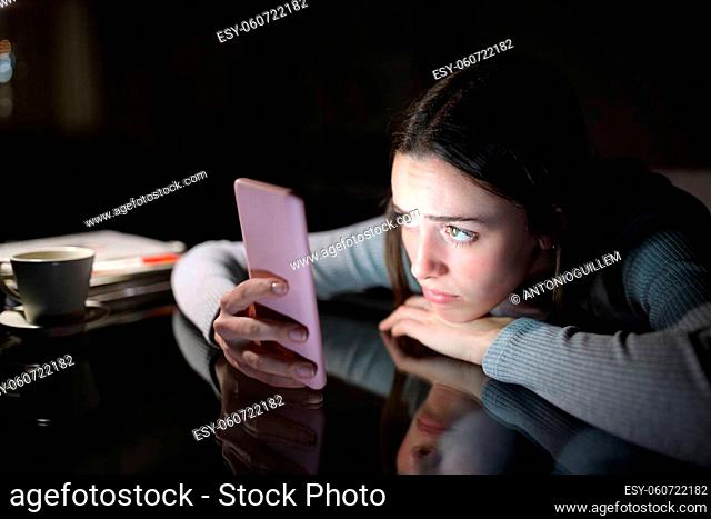 Worried woman checking smart phone content in the dark night at home
