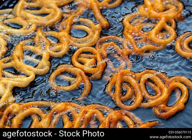 Frying Jalebi batter in oil. Red and orange-colored batter will be dipped into sugar syrup for a sweet taste. Jalebi is a popular sweet snack