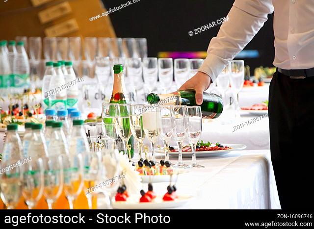 Waiter's hands pouring a drink into glasses