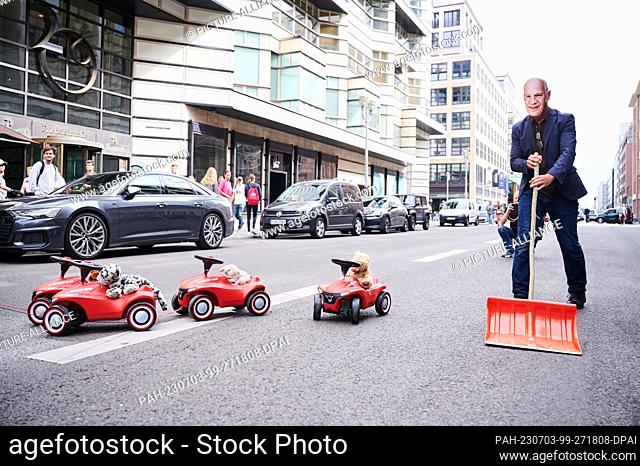 03 July 2023, Berlin: A demonstrator wearing a ""Kai Wegner mask"" symbolically sweeps the Bobby Cars out of the way on Friedrichstraße