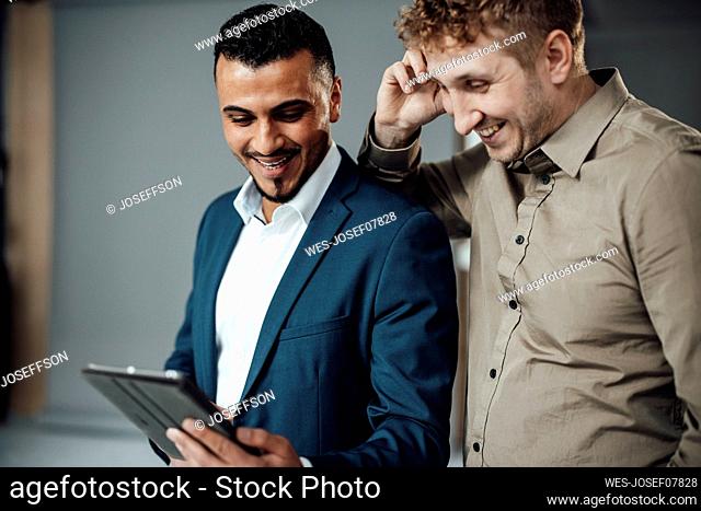 Happy businessman discussing over tablet PC with colleague in office