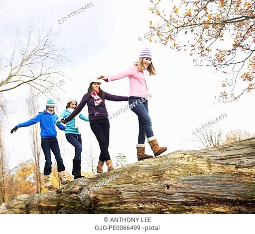 Girls crossing fallen log in a row