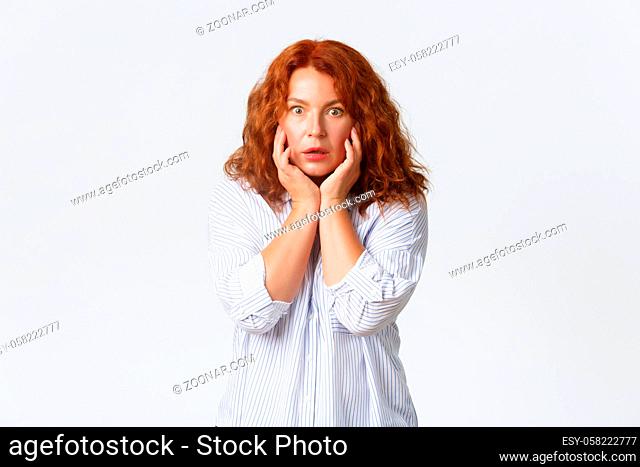 Shocked and concerned, worried redhead middle-aged woman stare at camera, holding hands on cheeks, spot new wrinkle. Anxious and concerned mother hear bad news