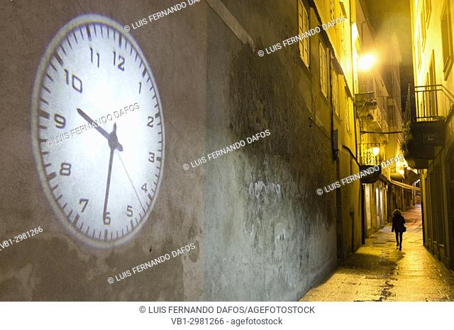 Lone woman walking on a dark alley and projection of big clock on an empty wall. Old Town of Viveiro, Lugo province, Galicia, Spain, Europe