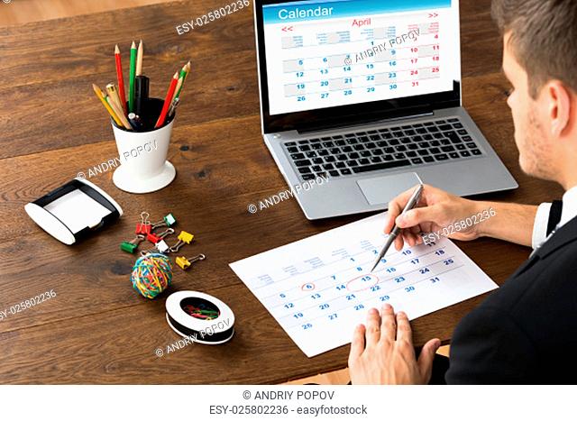 Close-up Of Businessman With Laptop Marking Date On Calendar