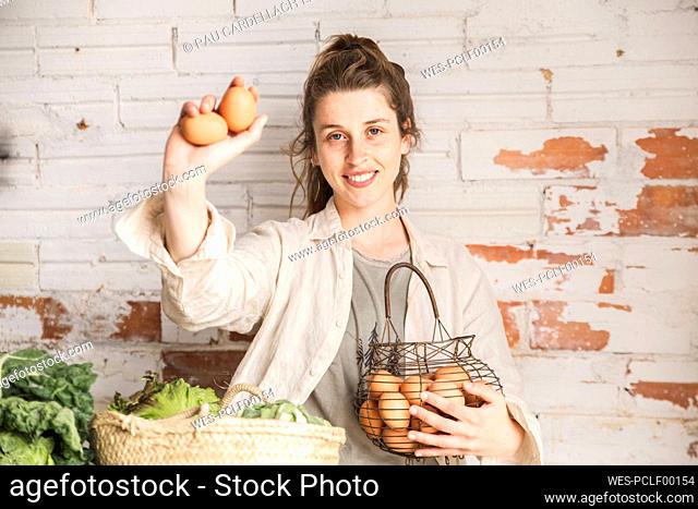 Smiling grocer showing eggs in front of brick wall