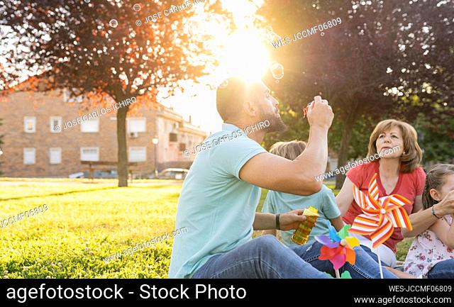 Man blowing bubbles sitting by family at park