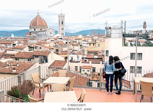 Rear view of lesbian couple standing of roof terrace looking at view of Giotto's Campanile and Florence Cathedral, Tuscany, Italy