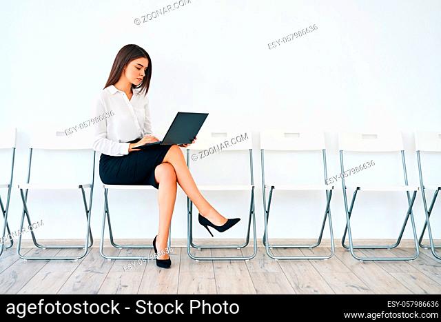 Pretty young business woman working on laptop sitting in empty conference hall prepare for business presentation. Employment or recruitment concept