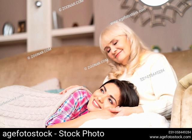 Smiling Brunette Enjoys Spending Time With Her Elderly Mother By Laying On Her Laps. Elderly Mother Gently Hugs Her Daughter