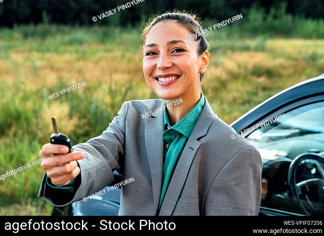 Happy beautiful saleswoman with key standing in front of car