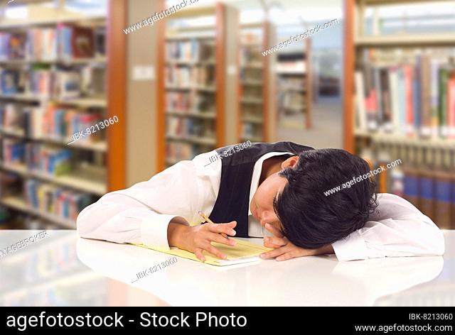 Young female mixed-race student stressed and frustrated in library with blank pad of paper
