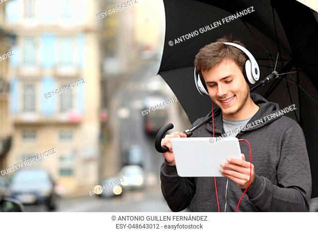 Happy teen watching online media in a tablet a rainy day walking in the street