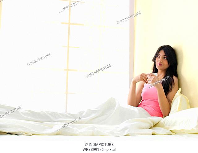 Girl sitting in bed with a cup of coffee