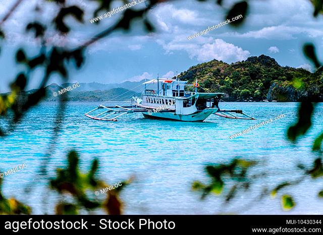 Tourism divers boat in blue cadlao lagoon framed by leaves. Island hopping tour, El Nido, Palawan, Philippines