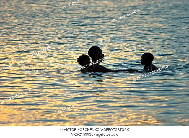 Bahamian mother with two kids bathing in ocean at sunset