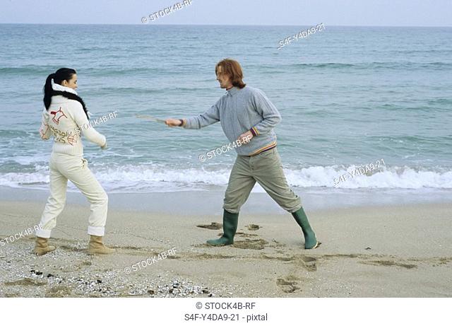 Young Couple fighting with little Sticks - Imitation of a Swordplay - Fun - Leisure Time - Beach