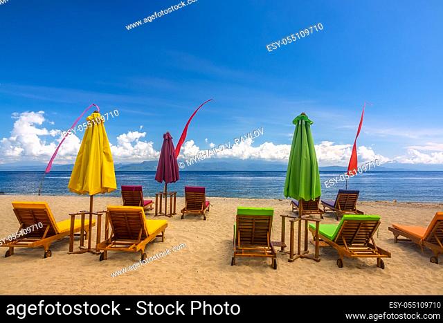 Tropical sandy beach. Empty deck chairs, closed beach umbrellas and blue sky with clouds