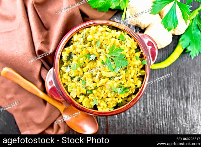Indian national dish kichari made of mung bean, rice, celery, spinach, hot pepper and spices in a bowl on a towel, ginger and spoon on wooden board background...
