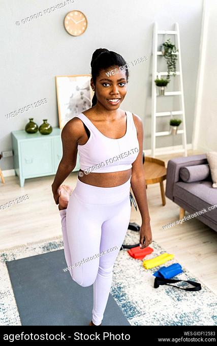 Smiling woman standing on one leg while exercising at home