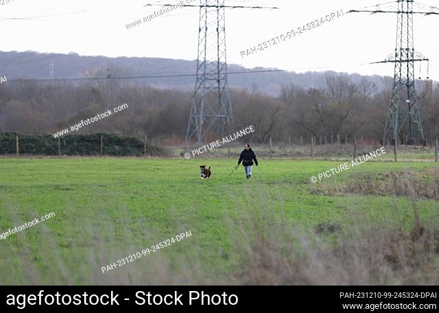 10 December 2023, North Rhine-Westphalia, Siegburg: A woman walks a dog in a meadow Photo: Sascha Thelen/dpa. - Siegburg/North Rhine-Westphalia/Germany