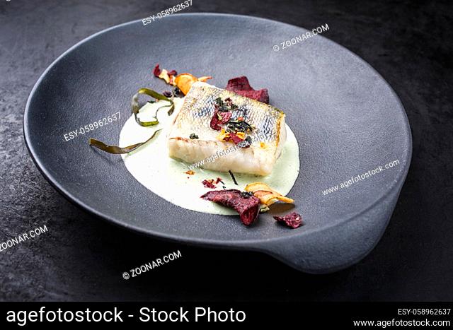 Traditional fried skrei cod fish filet with vegetable chips and algae in a lemon coconut sauce offered as close-up in a modern design plate with copy space