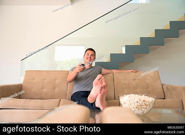 young handsome man enjoying free time watching television with popcorn in his luxury home villa