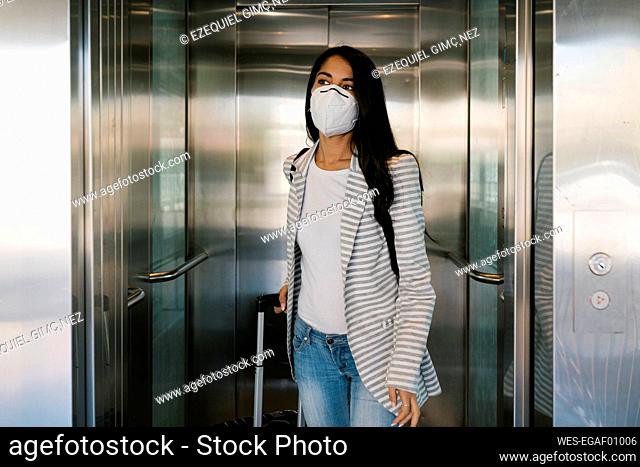 Woman wearing protective face mask walking out with luggage from elevator at station