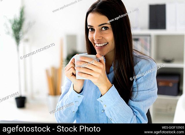 Smiling businesswoman drinking coffee while sitting at office