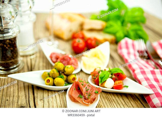 gemischte vorspeisenplatte mit parma parmesan tomaten oliven auf einem teller Holztisch