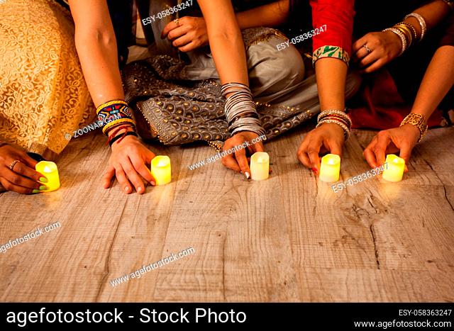 Women's hands holding lighted candles, sitting on floor. Indian holiday Diwali traditions. Closeup artificial candles on wooden floor