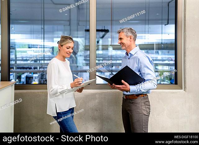Businessman with clipboard and businesswoman with digital tablet talking in factory office