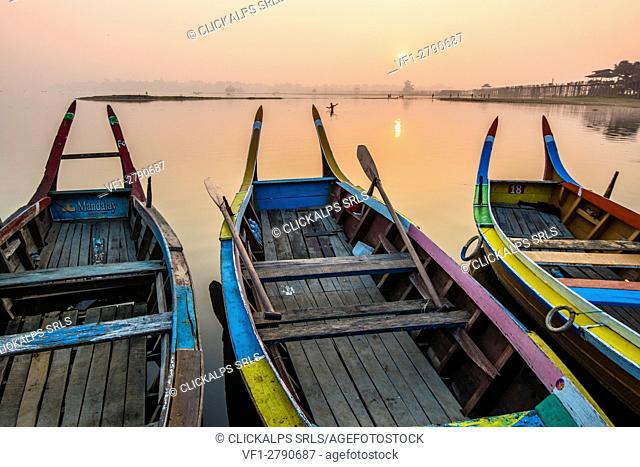 Amarapura, Mandalay region, Myanmar. Colorful boats moored on the banks of the Taungthaman lake at sunrise, with the U Bein bridge in the background
