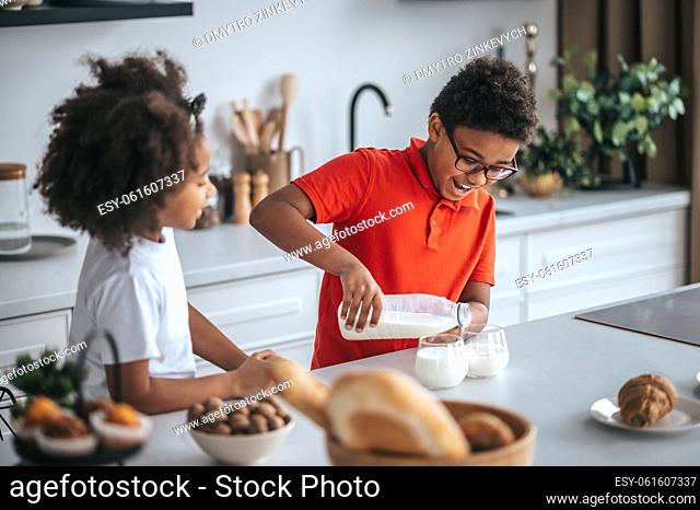 Breakfast time. A boy pouring milk for his sister in the kitchen