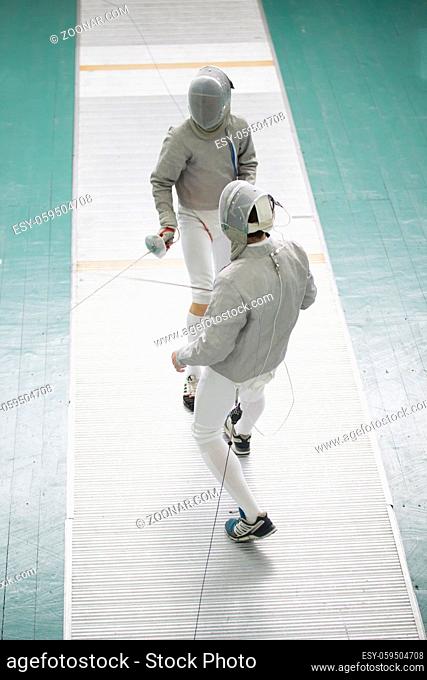 Two teenager fencers with swords on the fencing competition, telephoto shot