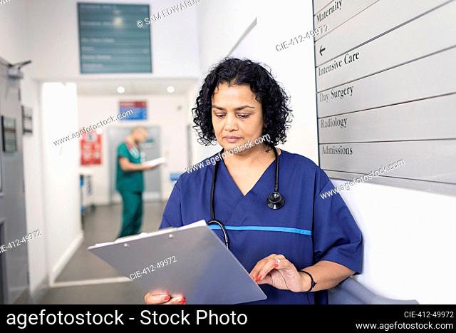 Female doctor with medical chart making rounds in hospital corridor