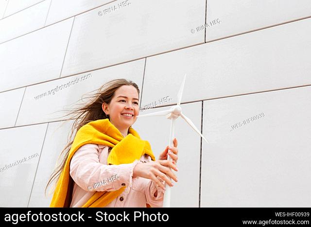 Happy woman with wind turbine model standing in front of wall
