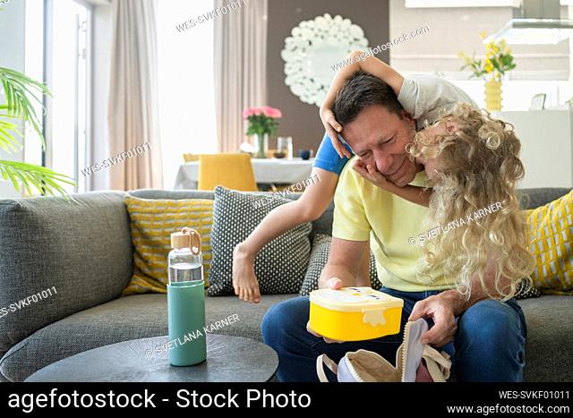 Father holding lunch box with playful daughter at home