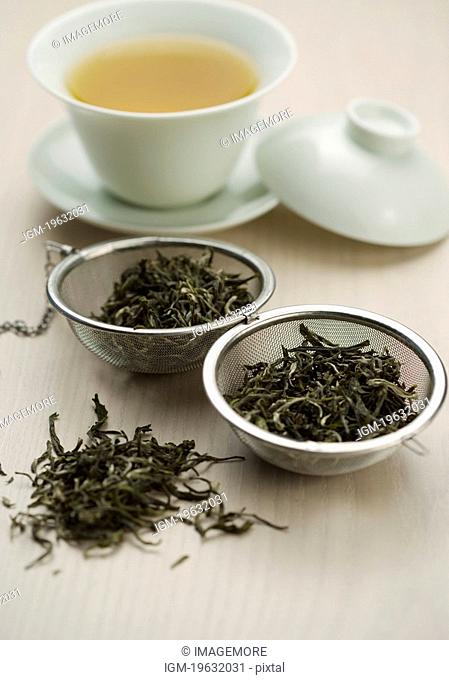 Dried tea leaves and tea strainer, cup of tea behind