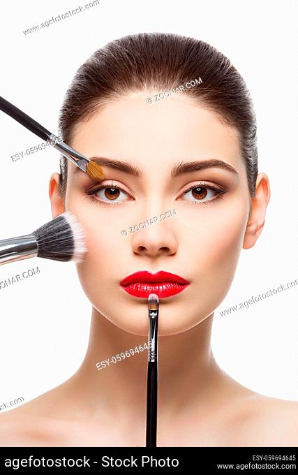 Closeup portrait of beautiful young woman with makeup brushes. Red lips. Isolated over white background