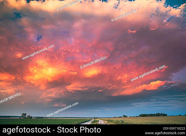 Dramatic Colorful Sky During Approaches Spring Storm Above Landscape With Rural Country Road Through Green Field And Meadow At Early Summer Season