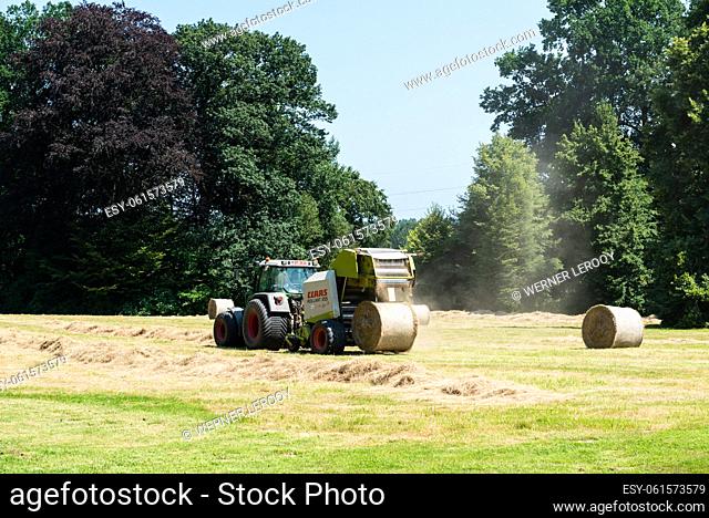 Lennik, Flemish Brabant Region - Belgium - 07 20 2021 Tractor forming bales of hay in a meadow
