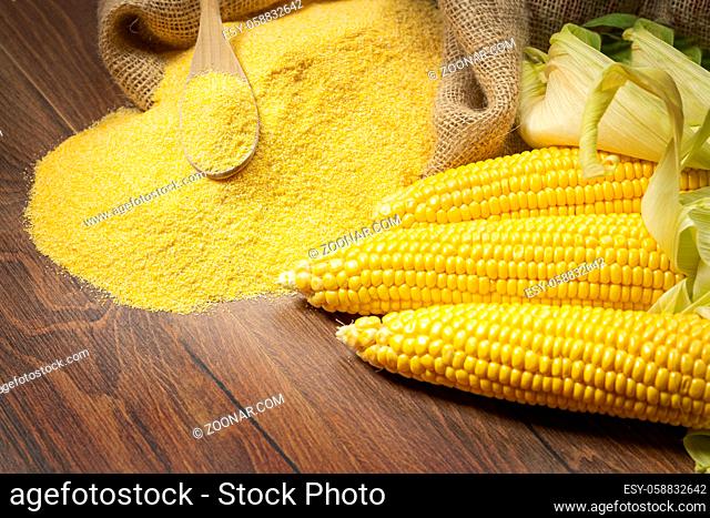 Ripe young sweet corn cob, on left stack cornmeal and spoon on top, wooden background, copy space.Gluten free food concept