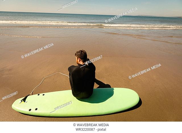 Surfer sitting on surfboard at beach