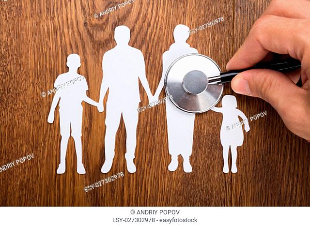 Person Holding Stethoscope On Family Papercut At Wooden Desk