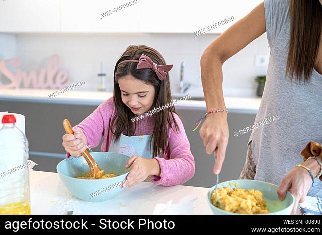 Daughter preparing muffin standing by mother in kitchen